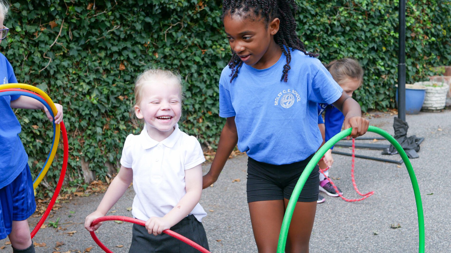 an older pupil playing with younger pupil with hula hoops on the playground