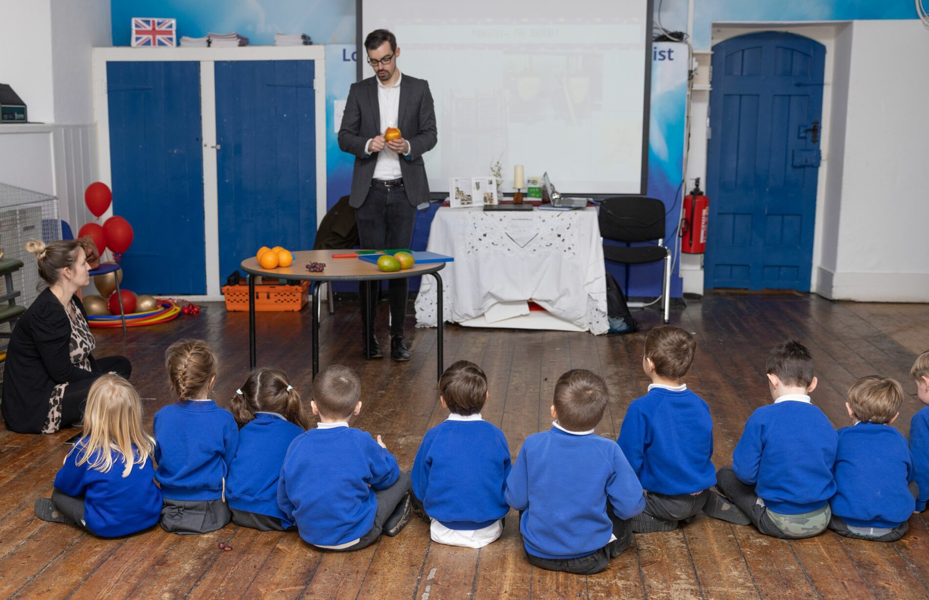 pupils sat on the floor looking at a man talking and demonstrating preparing fruit