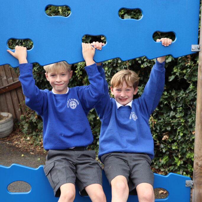 two pupils at sedleys primary school smiling and playing on the outdoors climbing frame