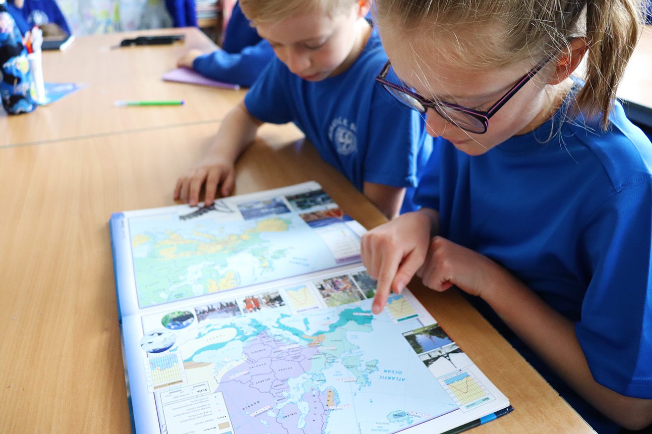 IMG_8520 two pupils looking at an atlas with one child pointing at spain