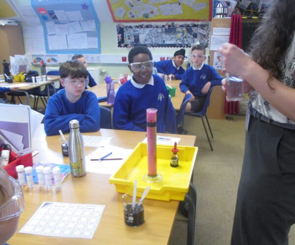 year 5 and 6 children watching a science experiment demonstrated by a teacher